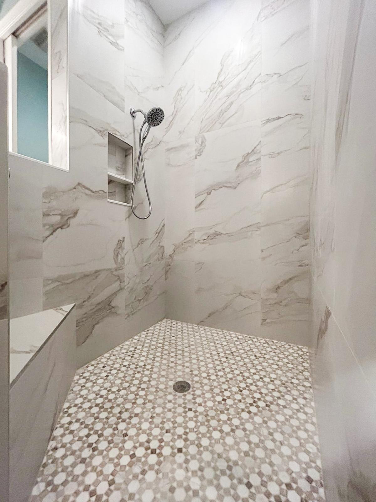 Finished shower with marble-look tile and mosaic floor